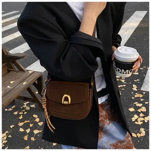 Detail of dark brown suede square bag with golden U-buckle worn on an autumn street