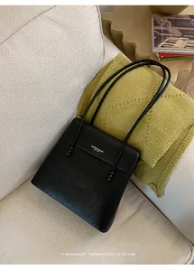 Detail of black lychee grain leather tote bag with gold logo on a cozy white sofa