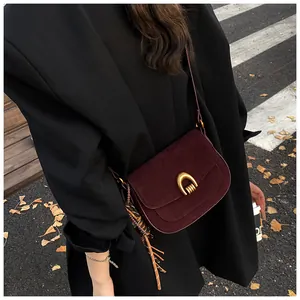 Detail of burgundy suede shoulder bag with gold hardware and woven fringe on black coat