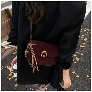 Detail of burgundy suede crossbody bag with gold buckle and fringe charm in autumn setting