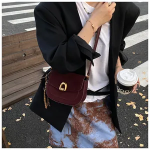 Detail of burgundy suede shoulder bag featuring a gold U-shaped lock and tassel accent