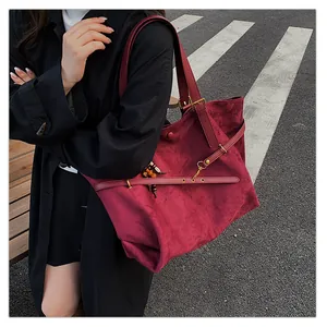 Close-up of a burgundy suede tote bag with a decorative bead charm in an outdoor setting