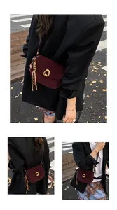 Detail of burgundy suede crossbody bag with gold U-shaped buckle and fringe pendant