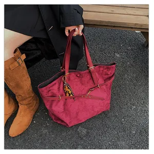 Close-up of burgundy suede tote bag with wooden bead charm and gold buckle detail