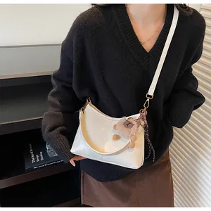 Detail of white glossy crescent bag with soft leather strap and cute bear charm