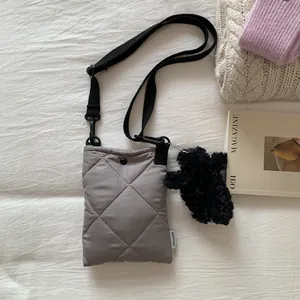Gros plan d'un sac bandoulière gris matelassé avec bandoulière réglable et breloque ours