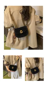 Detail of a black matte saddle bag with a golden U-shaped buckle on a khaki trench coat
