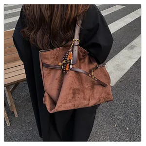 Detail of a brown suede tote bag featuring leather straps and bohemian beaded charm accessory