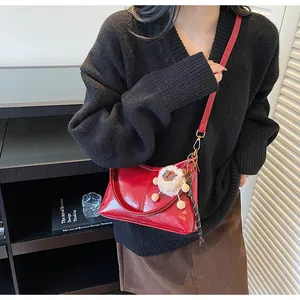 Detail of red glossy leather tote bag with cute plush lamb charm and crossbody strap