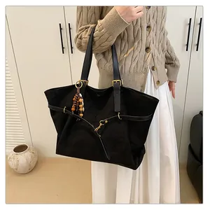 Detail view of a black suede tote bag with leather straps and vintage bead charm