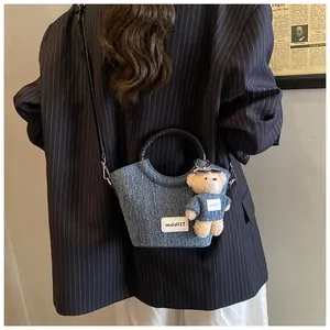 Chic denim bucket bag with plush bear charm and sleek black handle shown on model