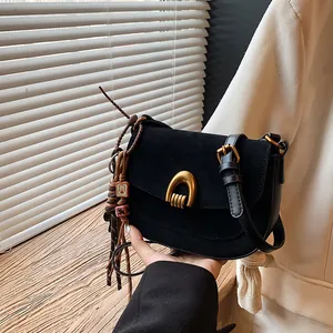 Minimalist black suede saddle bag with golden U-shaped buckle and woven charm