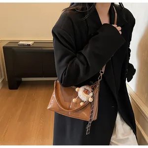 Caramel brown leather tote bag with white plush sheep pendant shown on person