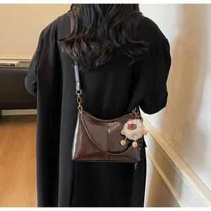 Model wearing dark brown glossy patent leather tote bag with cute plush sheep keychain