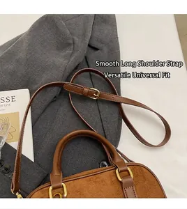 Detailed view of the brown suede bowling bag with leather handles and gold metal buckles