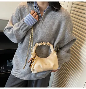 Detail of beige pleated handbag featuring a gold chain and colorful beaded charm strap