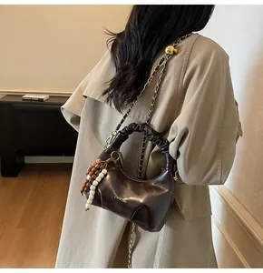 Detail of dark brown pleated leather bag with chain strap worn by a model in a trench coat