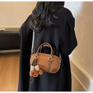Detail of a brown matte leather bowling bag with teddy bear pendant on a black coat