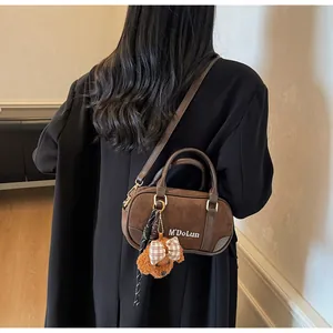 Close-up of brown suede bowling bag featuring a white logo and a cute teddy bear charm