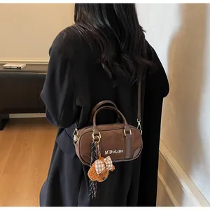 Detail of brown suede bowling bag with white text and cute plush bear charm accessory