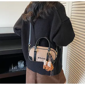 Close-up of brown bowling bag with black leather handles and plush teddy bear charm