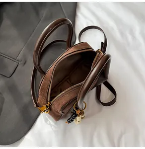 Detail of vintage brown suede Boston bag with gold hardware and beaded charm on white bedding