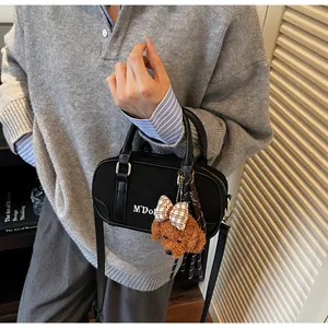 Detail of black canvas Boston bag with leather trim and brown teddy bear charm on strap