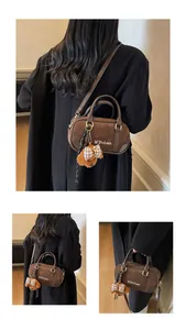 Detail of dark brown matte bowling bag with plush bear charm and golden hardware