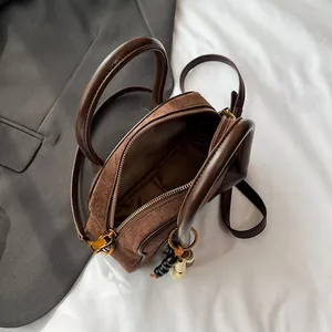 Brown suede patchwork Boston bag with wooden bead charm and top handles on a suit background