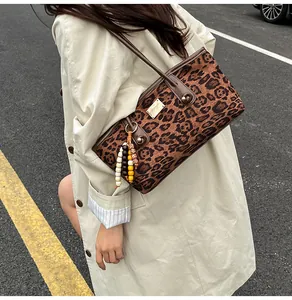 Detail of leopard print crossbody bag with golden logo plaque and beaded tassel