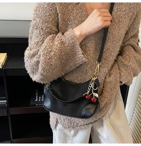 Detail of black nylon shoulder bag with cherry pendant and leather strap worn by model