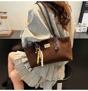 Detailed close-up of dark brown suede tote bag featuring silver plate and beaded tassel