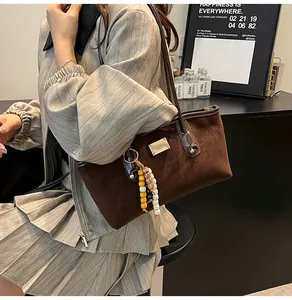 Detail of dark brown suede handbag featuring a silver brand plaque and beaded charm