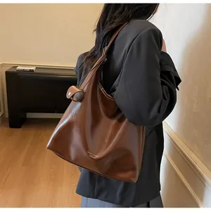 Detail view of brown leather tote bag worn by a model in a modern office setting