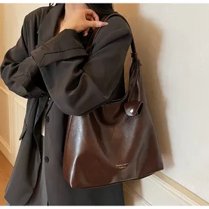 Detail of a dark brown leather bucket tote bag with metal buckle and shoulder strap