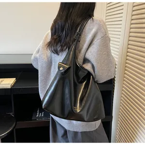 Detail of glossy black hobo shoulder bag with stylish knot strap and gold logo