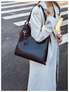 Détail d'un cabas en cuir noir brillant avec pompon en perles de bois sur modèle