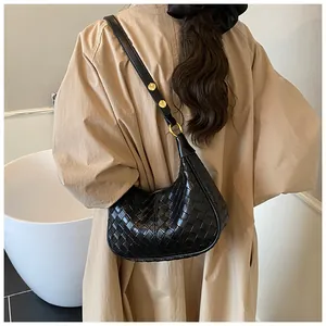Detailed back view of a black woven crescent bag with gold rivets on a trench coat