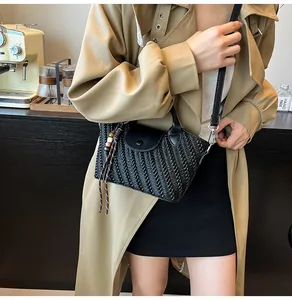 Detail der schwarzen geflochtenen Handtasche mit Quastenanhänger und Klappverschluss im Café