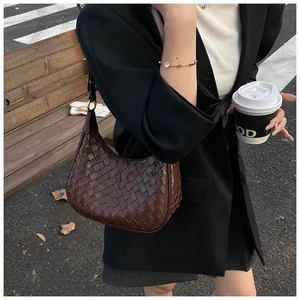 Detailed view of the woven dark brown crescent shoulder bag with metallic hardware buckle