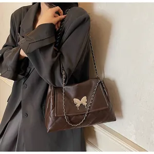 Detail of dark brown quilted tote bag featuring silver butterfly lock and chain strap
