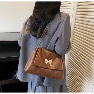 Detail of brown quilted tote bag with golden butterfly clasp and leather chain strap