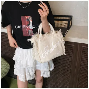 Detailed view of beige canvas tote with fringe edges and artistic Fashion lettering