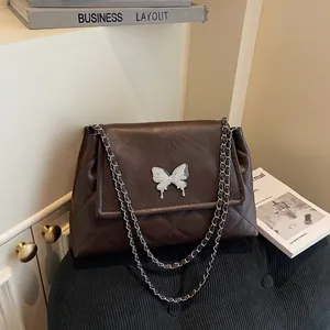 Quilted dark brown tote bag with butterfly ornament and chain strap on a black velvet stool