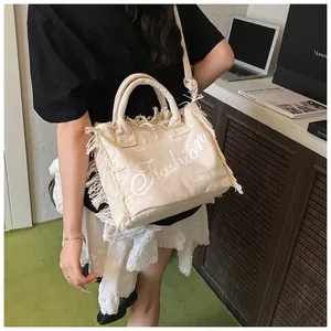Detail of off-white canvas tote with fringe edges and 'Fashion' text in urban setting