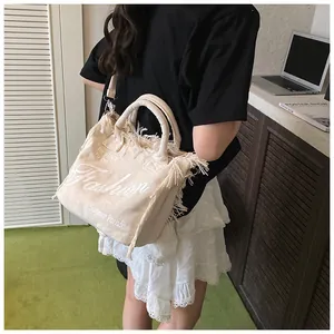 Detail view of off-white canvas tote bag featuring fringe edges and fashion text print