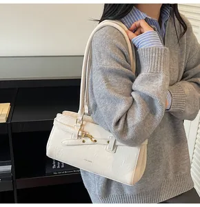 Detail view of cream leather shoulder bag with metallic buckle and slim strap on a model