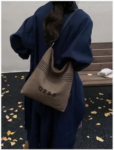 Outdoor shot of a coffee brown canvas bucket bag with QZBG lettering and black strap