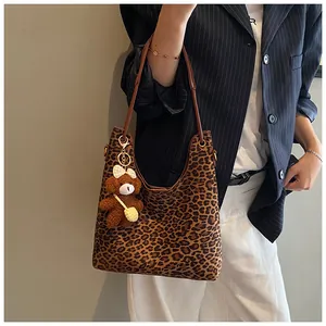 Leopard print hobo bag with brown strap and plush bear charm shown on a model