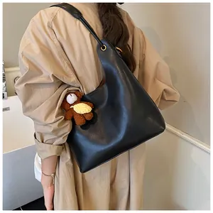 Lifestyle view of a black minimalist tote bag with a cute plush bear charm on the shoulder strap